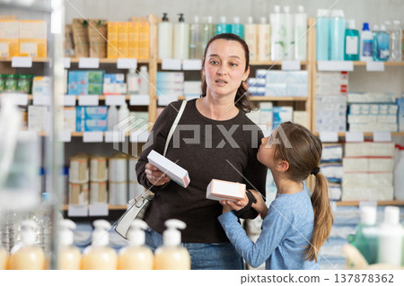 Woman with schoolgirl daughter are busy choosing tablet box at pharmacy Woman with schoolgirl daughter are busy choosing tablet box at pharmacy 137878362