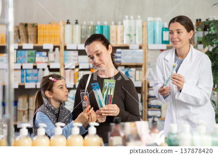 Woman with schoolgirl daughter are busy choosing toothbrush, pharmacist offer help in background 137878420