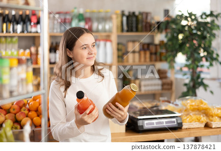 Teen girl hold packages bottles and choose consider juice in store Teen girl hold packages bottles and choose consider juice in store 137878421