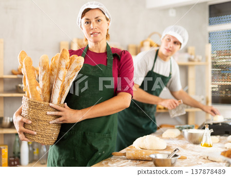 Adult woman baker with basket of baguettes Adult woman baker with basket of baguettes 137878489