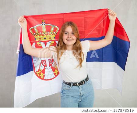 smiling girl in arms raised above head holds cloth of national flag of Serbia 137878519