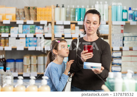 Woman with daughter in pharmacy scans QR code on gel for burns Woman with daughter in pharmacy scans QR code on gel for burns 137878532