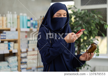 Young woman in niqab checking syrup medicine details on smartphone 137878553