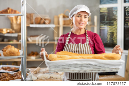 In working room of bakery, there is woman with baguettes in wicker basket in hands 137878557