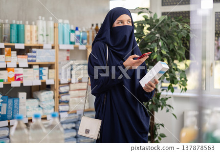 Young Muslim woman scanning QR-code on cream in drugstore 137878563