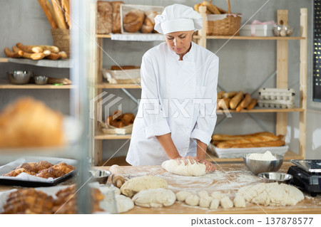 Woman works in bakery as baker, kneads dough, works with flour. 137878577