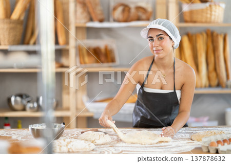Young female baker kneading dough on table Young female baker kneading dough on table 137878632