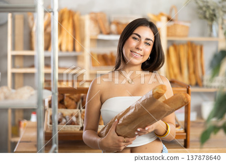 Positive young girl holding baguettes in paper bag Positive young girl holding baguettes in paper bag 137878640