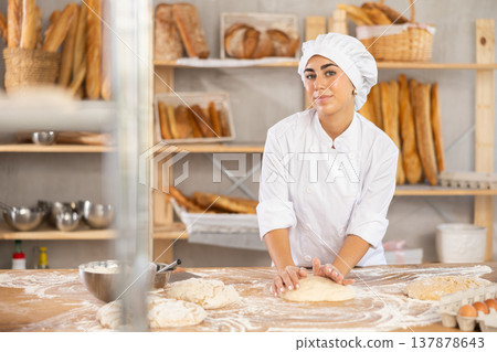 Young woman baker kneads the dough in bakery Young woman baker kneads the dough in bakery 137878643