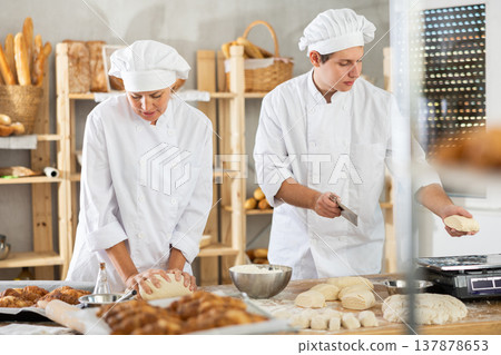 Male and female bakers knead dough, cut and weigh pieces 137878653