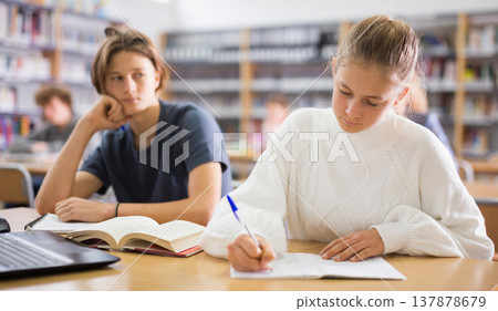 Girl and boy preparing for exams in library Girl and boy preparing for exams in library 137878679