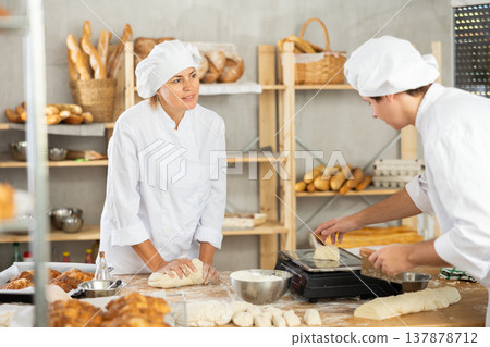 Male and female bakers knead dough, cut and weigh pieces Male and female bakers knead dough, cut and weigh pieces 137878712