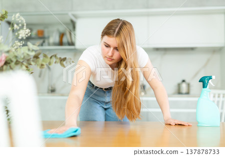 in kitchen,positive housewife in casual clothes holds rag in hands and cleans surface of table in kitchen,positive housewife in casual clothes holds rag in hands and cleans surface of table 137878733