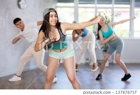 Young girl in ball cap and teenagers actively move and dance hip hop at choreography lesson Young girl in ball cap and teenagers actively move and dance hip hop at choreography lesson 137878737