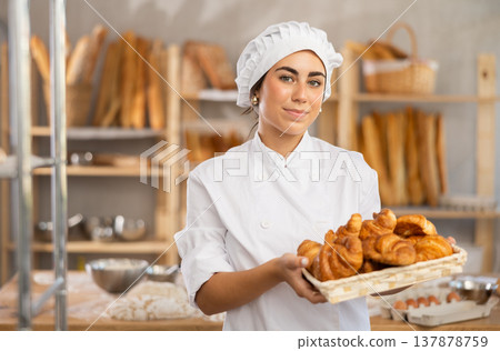 Young saleswoman displays croissants in square wicker basket Young saleswoman displays croissants in square wicker basket 137878759