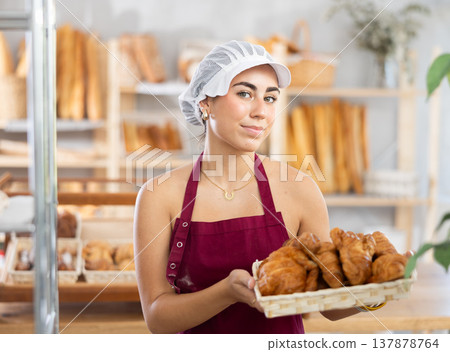 Young saleswoman displays croissants in square wicker basket Young saleswoman displays croissants in square wicker basket 137878764
