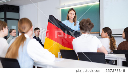 High school teacher holds the flag of Germany in her hands and talks about this country in geography lesson 137878846