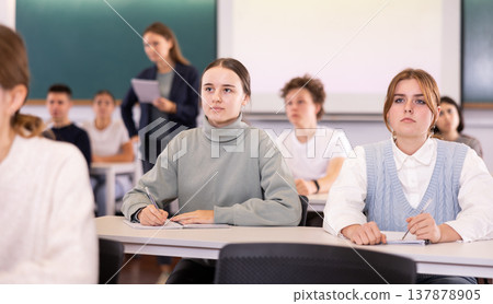 Girl and boy sitting at lesson in classroom, teacher standing 137878905