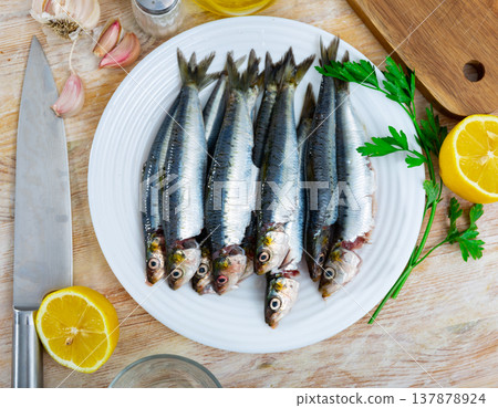 Fresh sardines lying on plate with lemon, parsley and garlic Fresh sardines lying on plate with lemon, parsley and garlic 137878924
