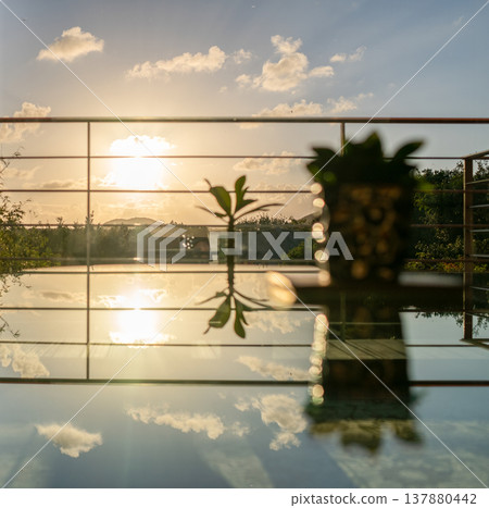 The image of the sunset seen from the window, the glass, and the sky reflected in the water basin. 137880442