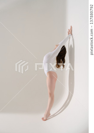 Elegant woman in a white leotard arching her back against a wall Elegant woman in a white leotard arching her back against a wall 137880792