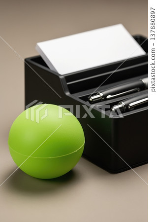 Green stress ball beside black desk organizer with pens and business cards Green stress ball beside black desk organizer with pens and business cards 137880897