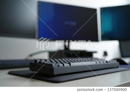 Mechanical keyboard in foreground with multiple monitors blurred in modern setup 137880900