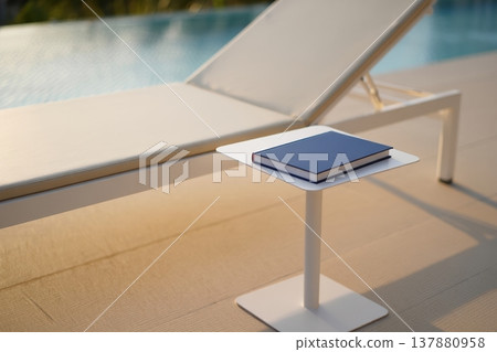 Solitary blue notebook on a poolside lounge chair table at golden hour Solitary blue notebook on a poolside lounge chair table at golden hour 137880958