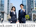 Japanese men and women in business suits looking determined amidst falling cherry blossoms in a city skyline: A springtime image of new graduates entering the workforce (AI generated) 137881159