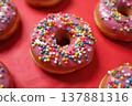 Pink frosted donuts with colorful sprinkles arranged on a vibrant red surface 137881316