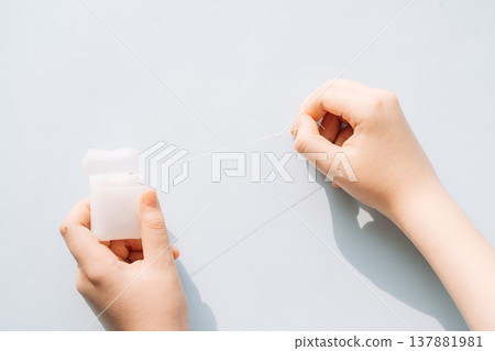 Child hands holding dental floss container and pulling floss on light blue background, oral hygiene concept Child hands holding dental floss container and pulling floss on light blue background, oral hygiene concept 137881981