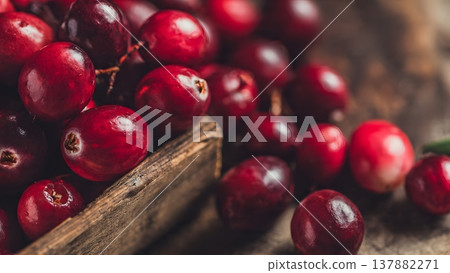 Close-up of vibrant red cranberries spilling from a rustic wooden crate, highlighting their texture and freshness. 137882271