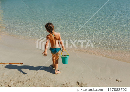 rear view of a child going to take water in plastic sand bucket in the sea rear view of a child going to take water in plastic sand bucket in the sea 137882702