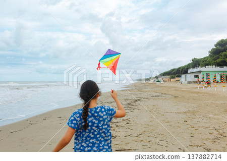 rear view of dark haired child flying a kite on the beach rear view of dark haired child flying a kite on the beach 137882714