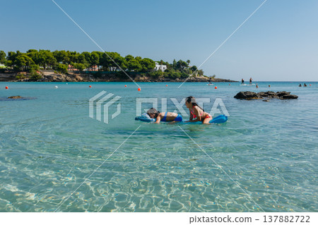 wide angle view of two girls swimming on a pool float on a sunny day in the sea 137882722