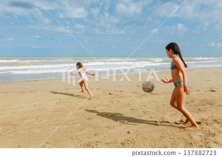 two girls in the swimsuit running on the beach playing with a ball two girls in the swimsuit running on the beach playing with a ball 137882723
