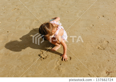 upper view of a child sitting on a beach drawing on sand 137882724