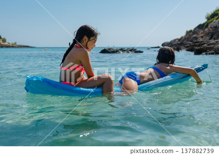 two girls swimming on a pool float on a sunny day in the sea two girls swimming on a pool float on a sunny day in the sea 137882739