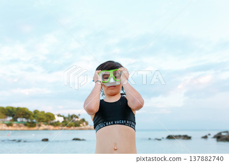 portrait of a girl putting on big swimming goggles while standing on a beach portrait of a girl putting on big swimming goggles while standing on a beach 137882740