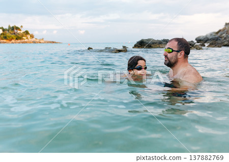 dad and daughter swimming together in crystal blue sea 137882769