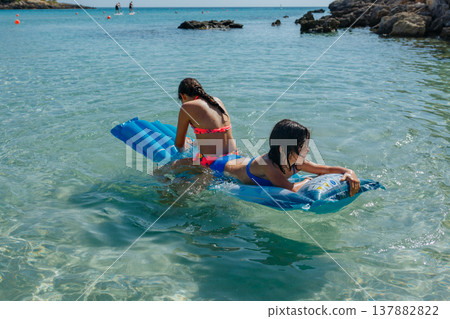 high angle view of two girls on pool float swimming on a sunny day in the sea high angle view of two girls on pool float swimming on a sunny day in the sea 137882822