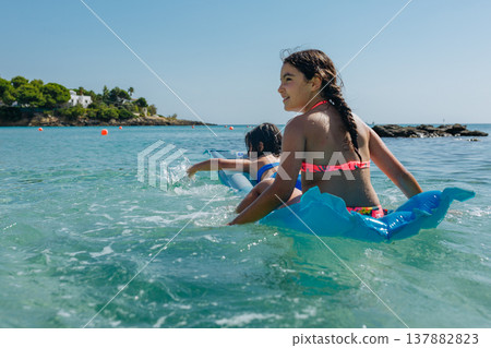 two girls on pool float swimming on a sunny day in the sea two girls on pool float swimming on a sunny day in the sea 137882823