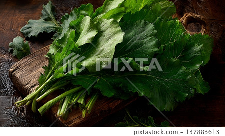 A bunch of fresh, vibrant mustard greens with water droplets, artfully arranged on a rustic wooden surface. 137883613