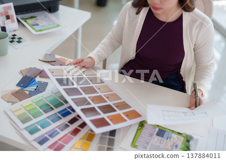 Asian adult woman designer selects color swatches material samples architectural blueprints plans home renovation creative diligent focused work modern office studio workspace 137884011