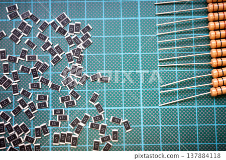 Surface mount resistors and through hole resistors on cutting mat, electronic components comparison background Surface mount resistors and through hole resistors on cutting mat, electronic components comparison background 137884118