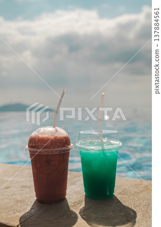 Two chilled drinks on pool edge with calm ocean horizon and soft sky creating tropical travel refreshment scene Two chilled drinks on pool edge with calm ocean horizon and soft sky creating tropical travel refreshment scene 137884561