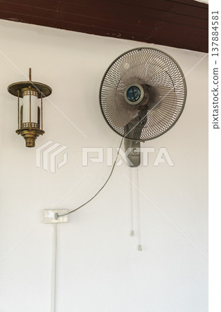 Wall mounted electric fan on white wall interior, household cooling appliance in home or apartment during hot weather Wall mounted electric fan on white wall interior, household cooling appliance in home or apartment during hot weather 137884581