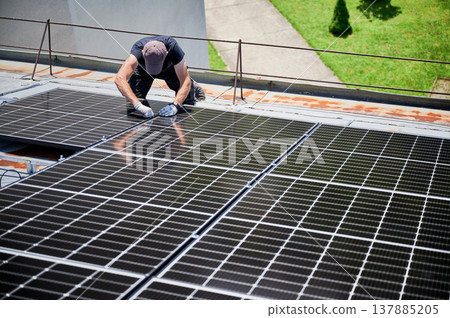 Worker building photovoltaic solar panel system on rooftop of house. Man engineer installing solar module with help of wrench outdoors. Alternative and renewable energy generation concept. Worker building photovoltaic solar panel system on rooftop of house. Man engineer installing solar module with help of wrench outdoors. Alternative and renewable energy generation concept. 137885205