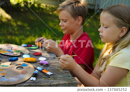 Children find canvas in nature, painting rocks with playful designs to give as their own handmade keepsakes. Children find canvas in nature, painting rocks with playful designs to give as their own handmade keepsakes. 137885252