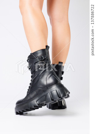 Legs of a woman in black leather boots from a new collection on a white background, legs of a girl in fashionable leather boots spring 2022. 137886722